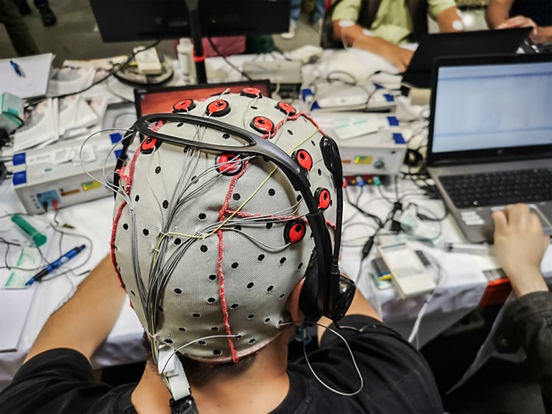 Person using a brain-computer interface, wearing an EEG cap connected to a laptop