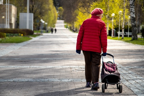 Older woman walking with rolling shopping bag.