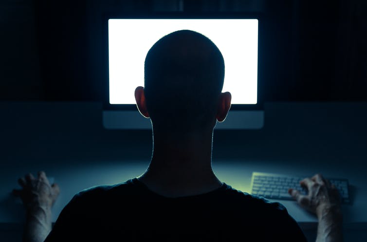 Picture of a man from behind staring at a computer screen.